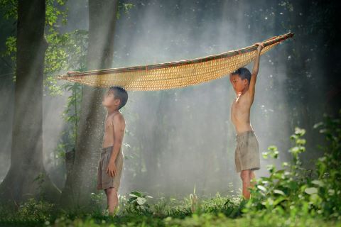 Two brothers standing by with a bamboo boat on a head in rural Thailand.